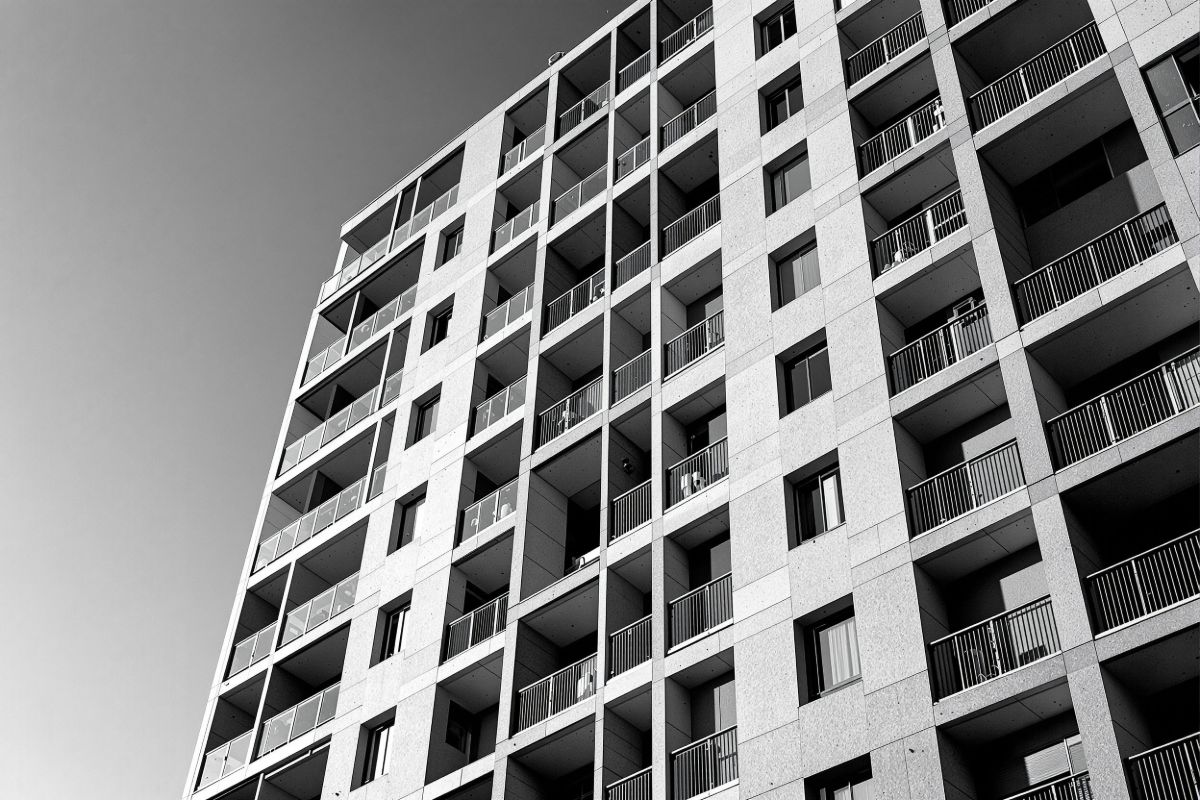 Fachada de un edificio de viviendas recién terminado en ángulo bajo, con la
            retícula de balcones marcada por la luz rasante de la tarde.