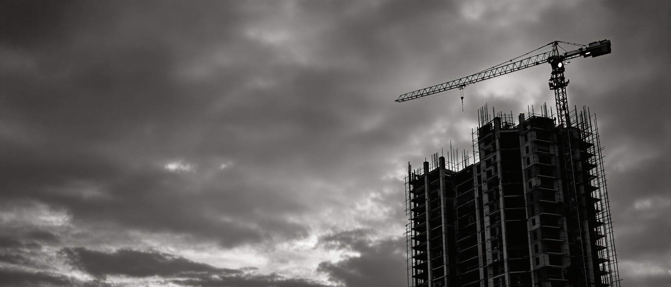 Estructura de un edificio de viviendas en construcción al anochecer, con la
        silueta de una grúa torre recortada contra el cielo.